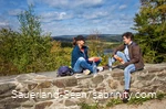 Zwei Frauen machen Rast auf einer Mauer mit Seeblick